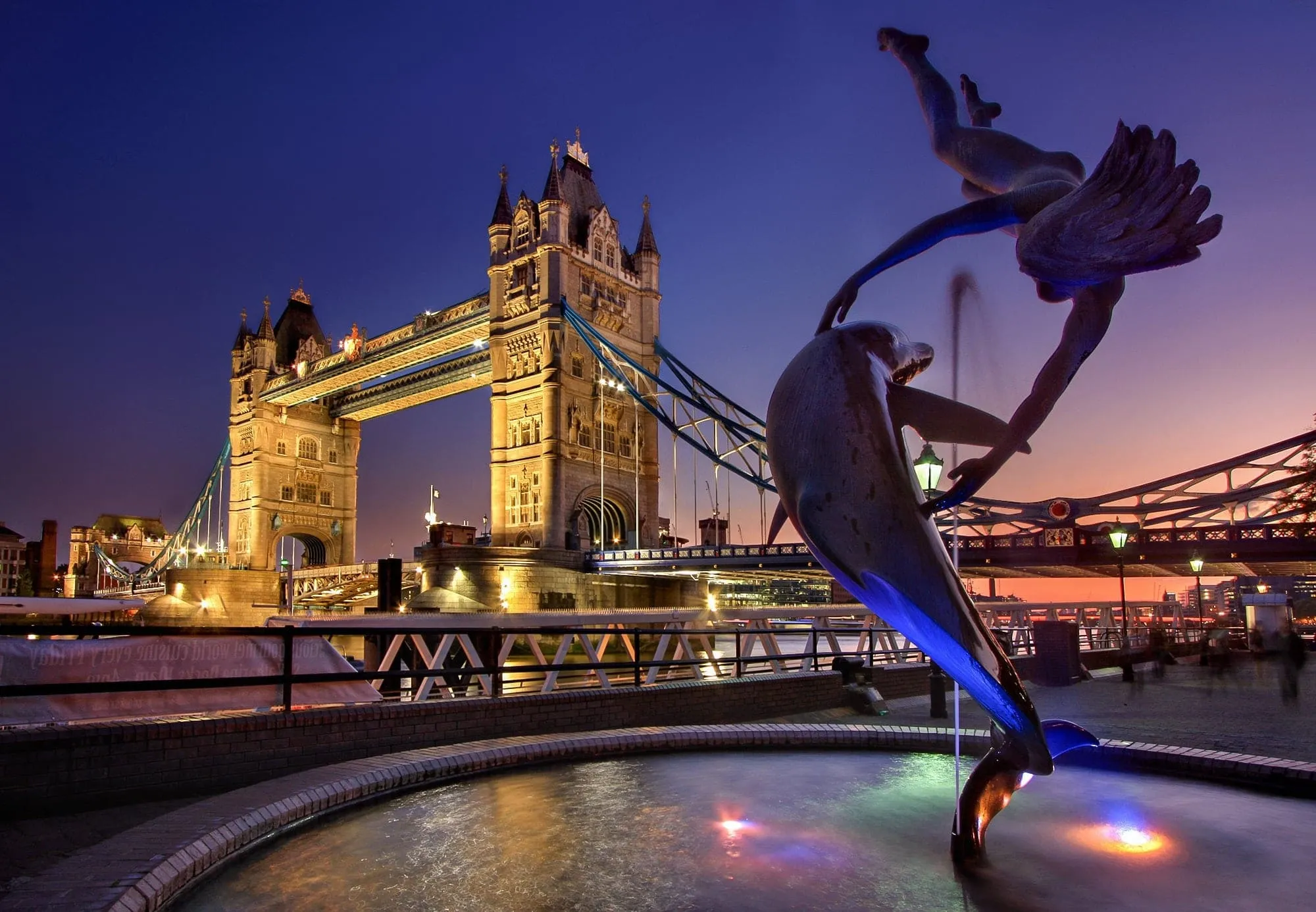 Tower Bridge lit up at twilight, seen from the Thames riverside